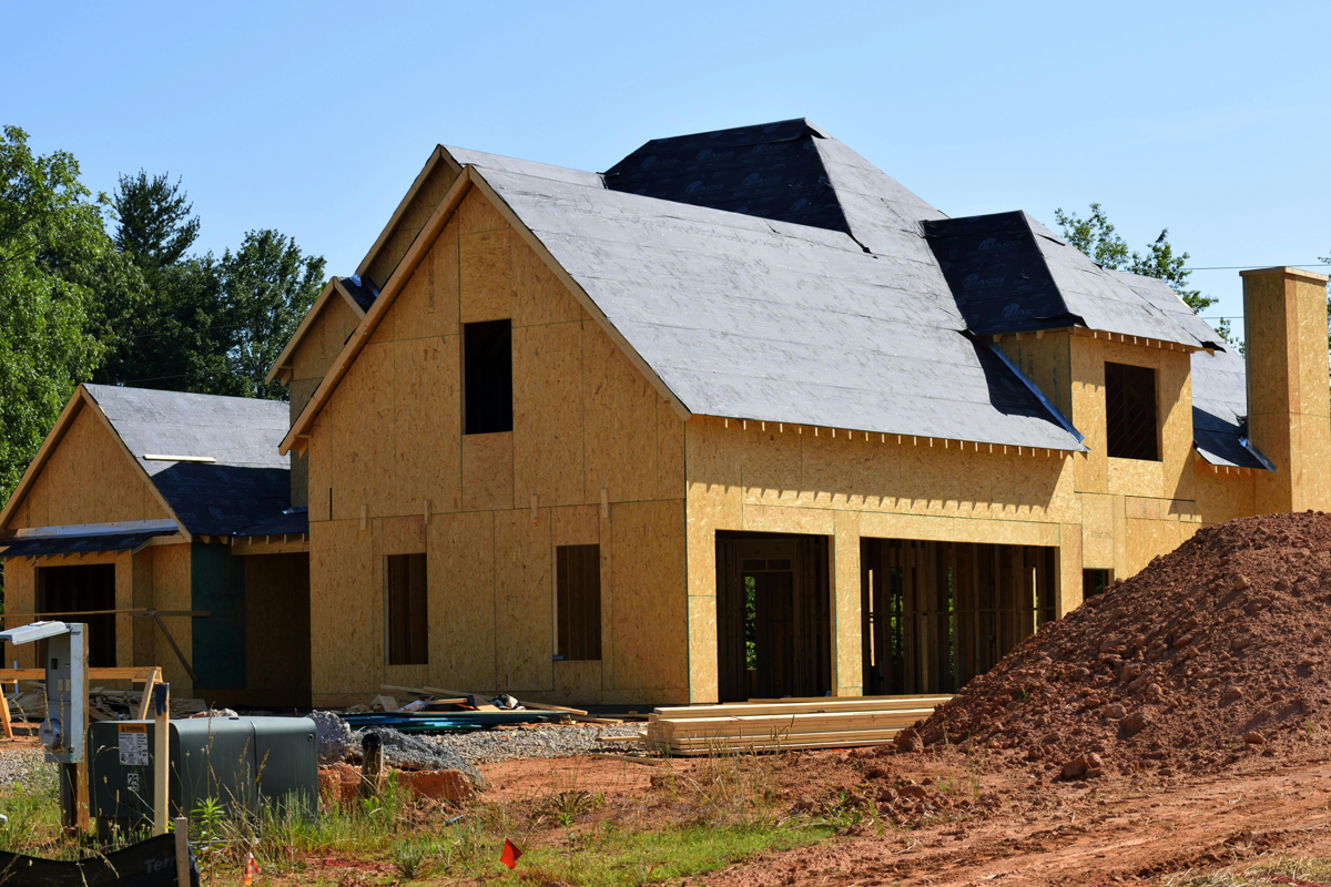 New home construction showing wooden framing and roof underlayment with uninstalled windows and doors at a Texas residential development site.