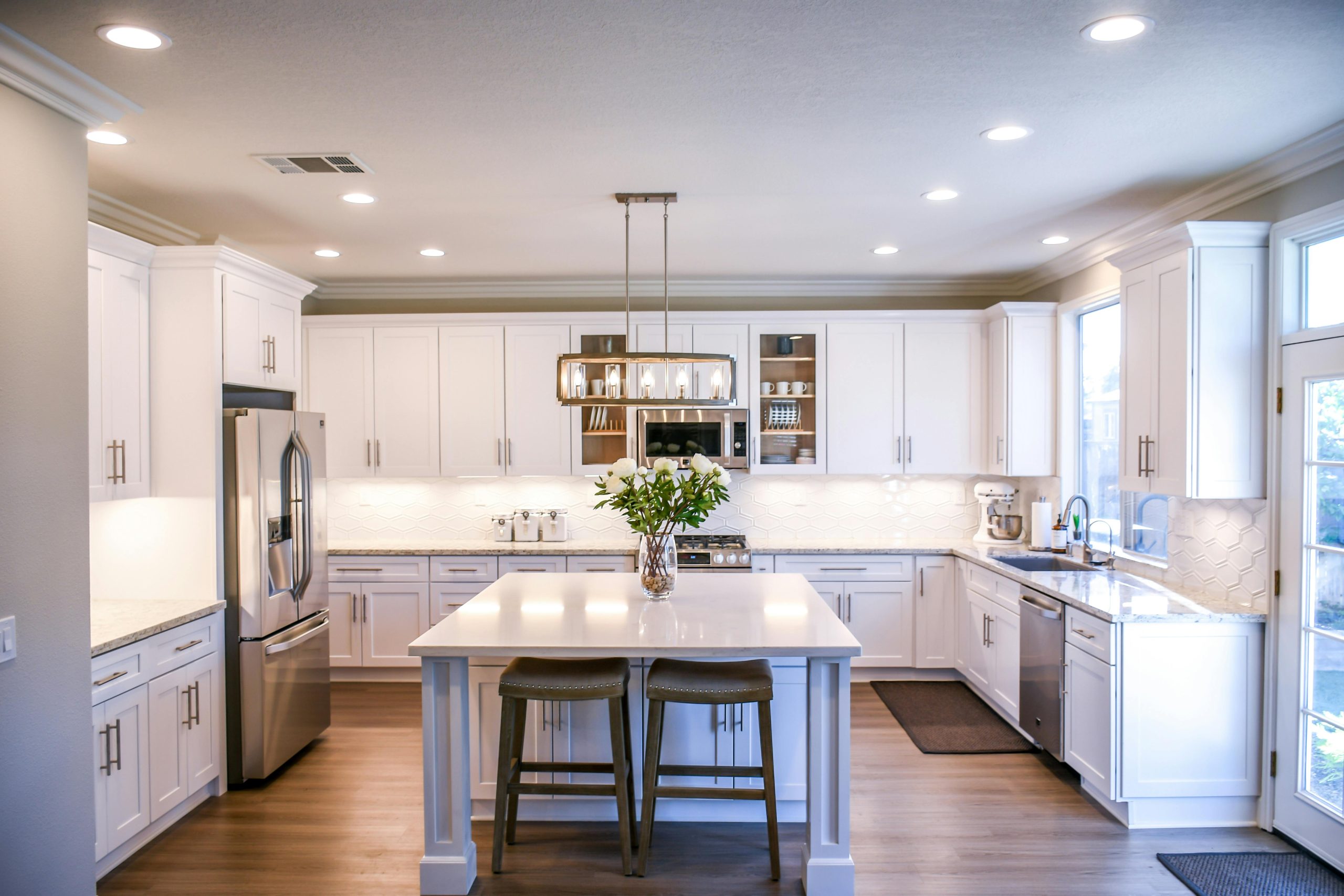 Bright modern kitchen with white cabinetry, stainless steel appliances, center island with bar stools, and hardwood flooring under natural light.