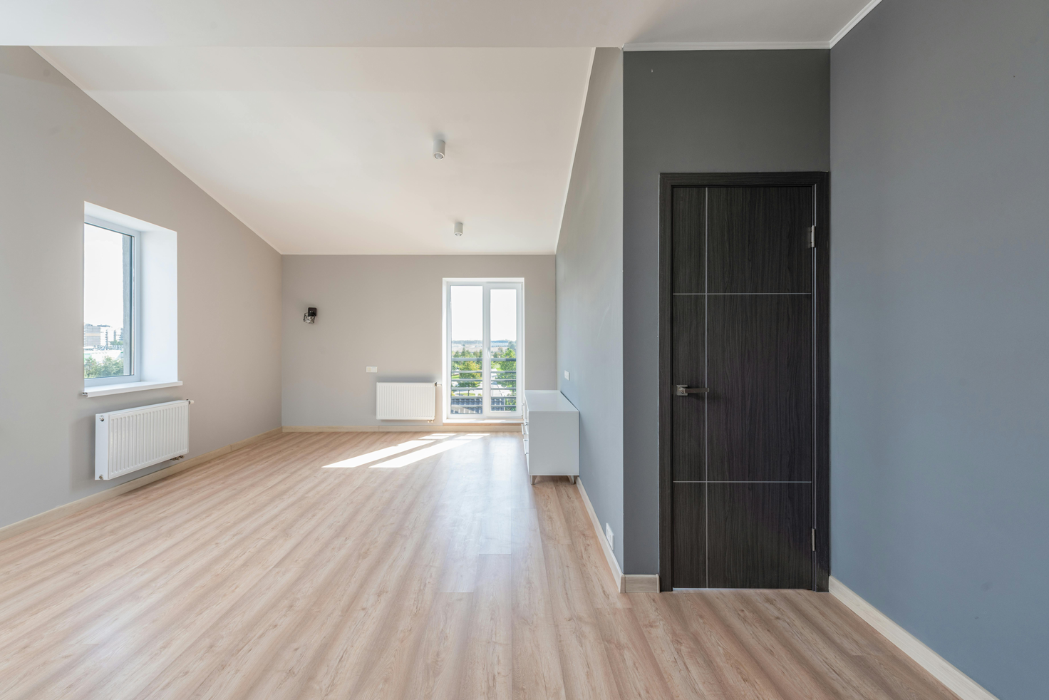 Bright, modern empty room with wood laminate flooring, large windows, and glass door leading to balcony in a newly renovated Houston property.