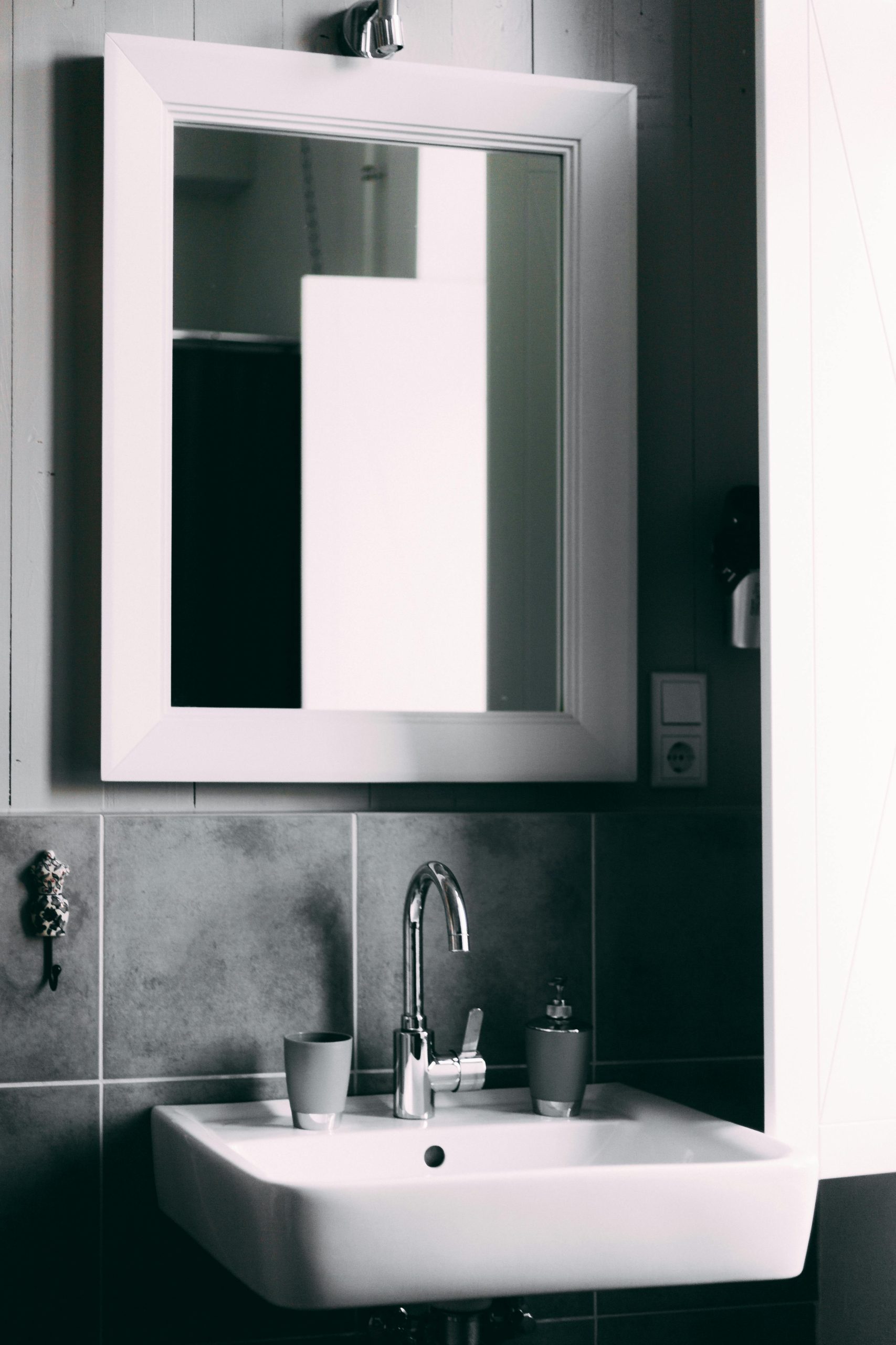 Modern minimalist bathroom featuring white ceramic sink, chrome faucet, framed mirror, and gray tiled backsplash with wooden accent wall.