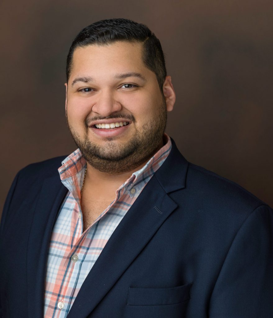 Professional real estate agent from Texas Signature smiling in navy blazer and plaid shirt against neutral background