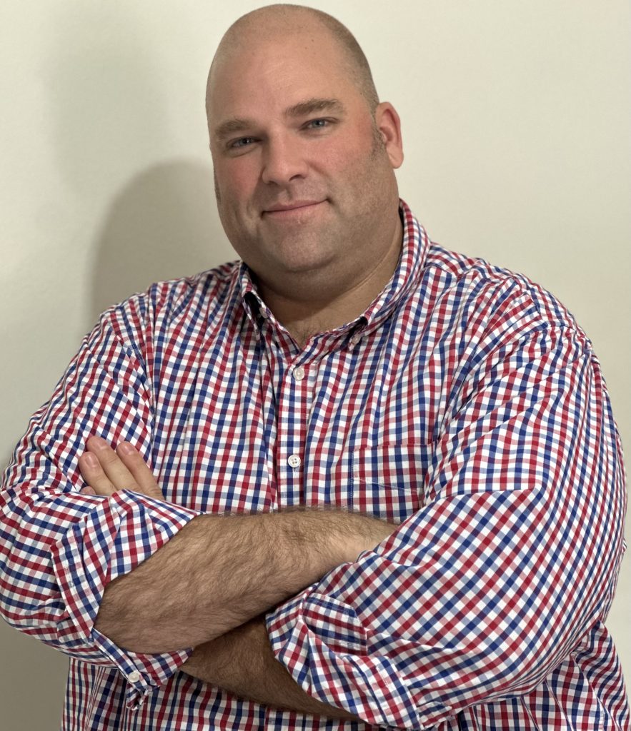 Professional real estate agent from Texas Signature wearing a red, white, and blue checkered shirt with arms crossed, ready to assist clients.